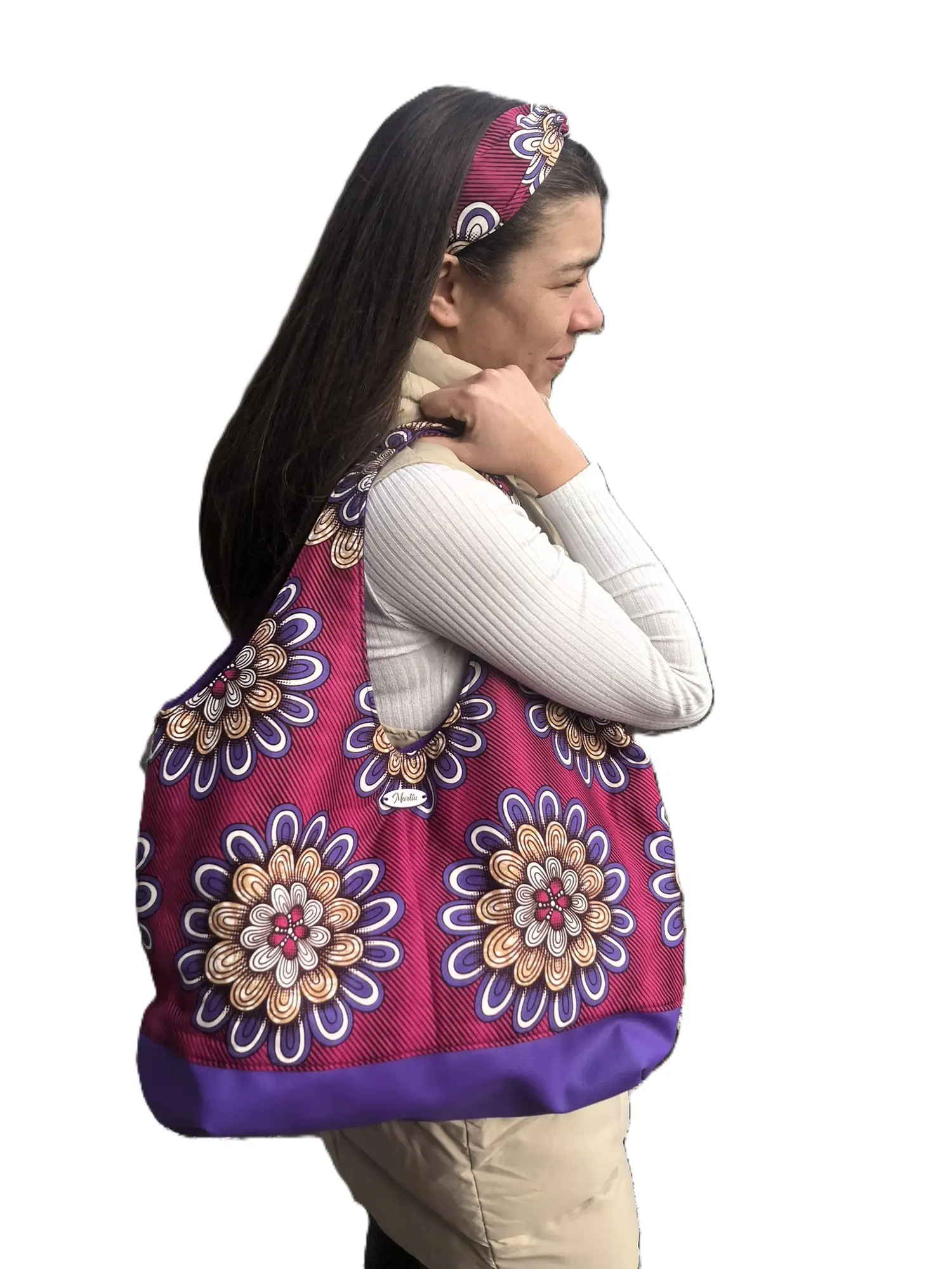Una mujer lleva al hombro un bolso de gran capacidad de la marca MARTIU que destaca por su base de color violeta intenso y un cuerpo de tela con grandes flores estampadas, combinando comodidad y diseño artesanal de autor.