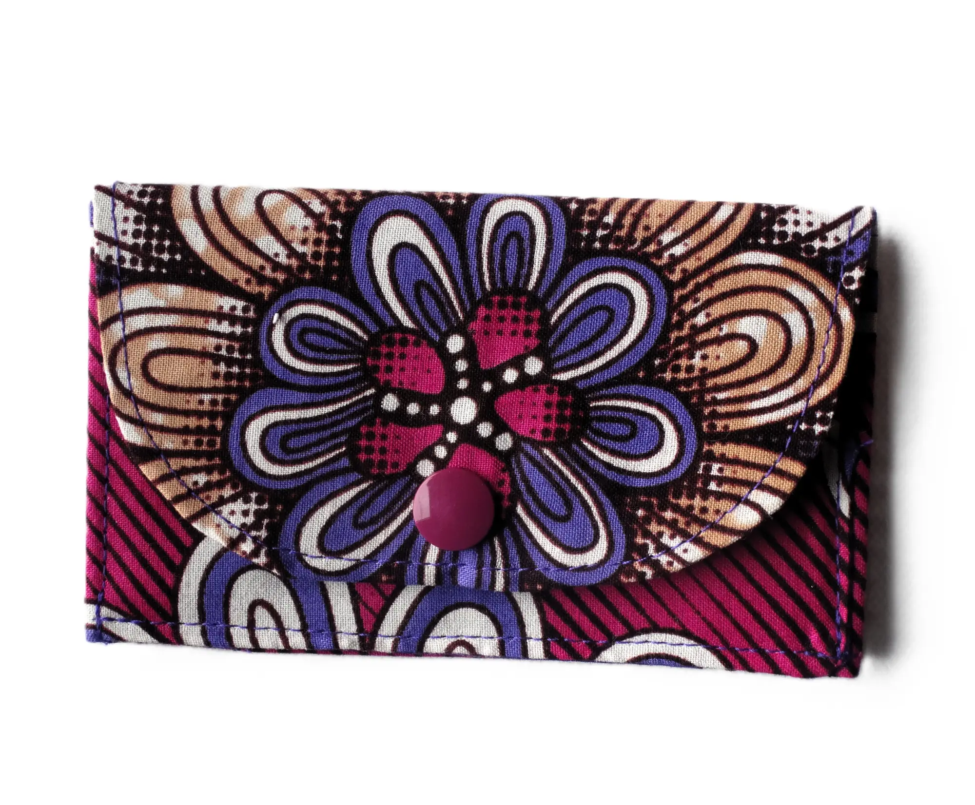 Monedero pequeño de MARTIU confeccionado en tela con un patrón de flor mandálica central en colores fucsia y violeta sobre fondo de rayas, con un cierre de botón a presión en color uva que complementa el estilo artesanal.