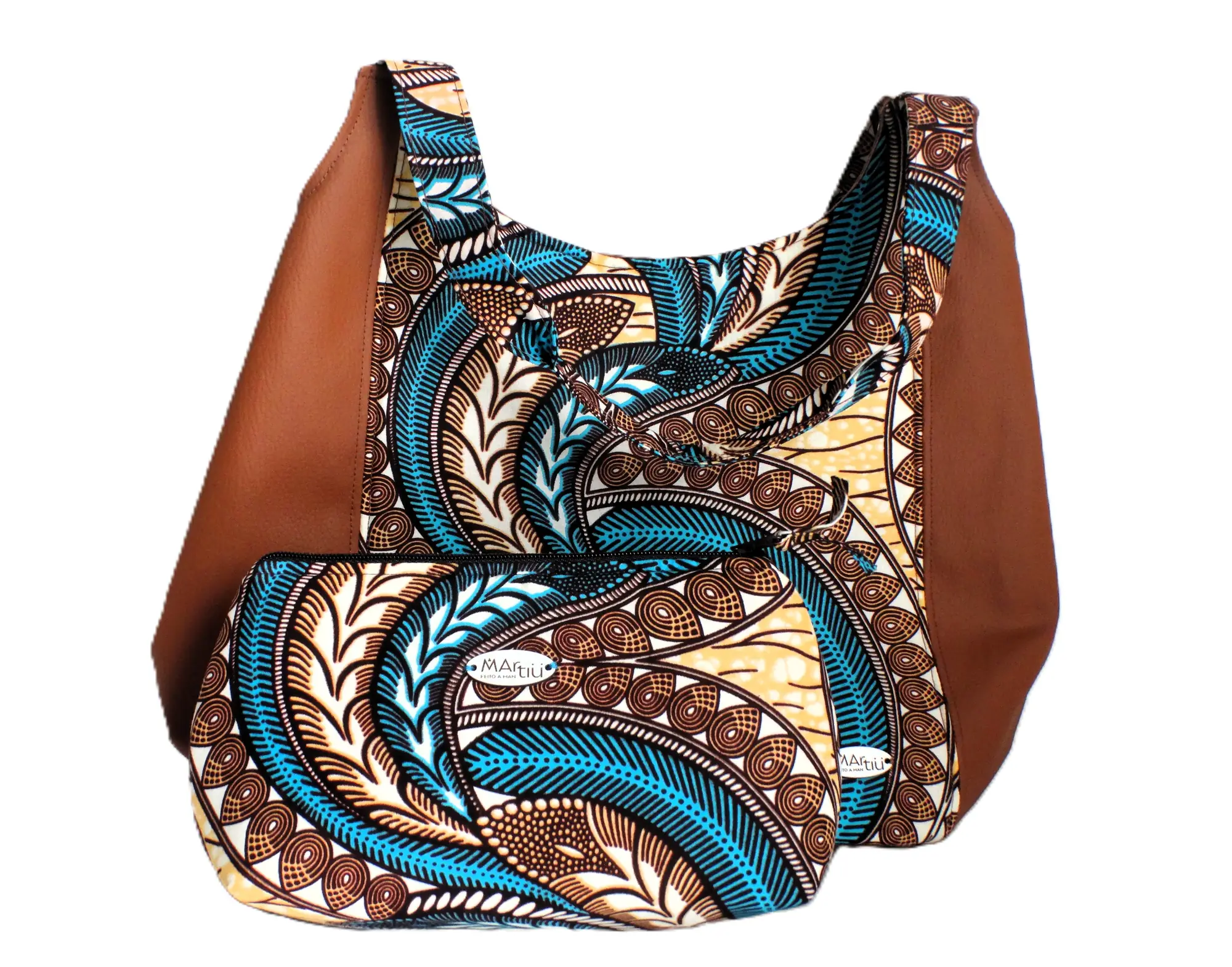 Un conjunto coordinado de la marca MARTIU que incluye un bolso de hombro con laterales de cuero marrón y un neceser a juego, ambos compartiendo el patrón textil de plumas estilizadas en azul y ocre.