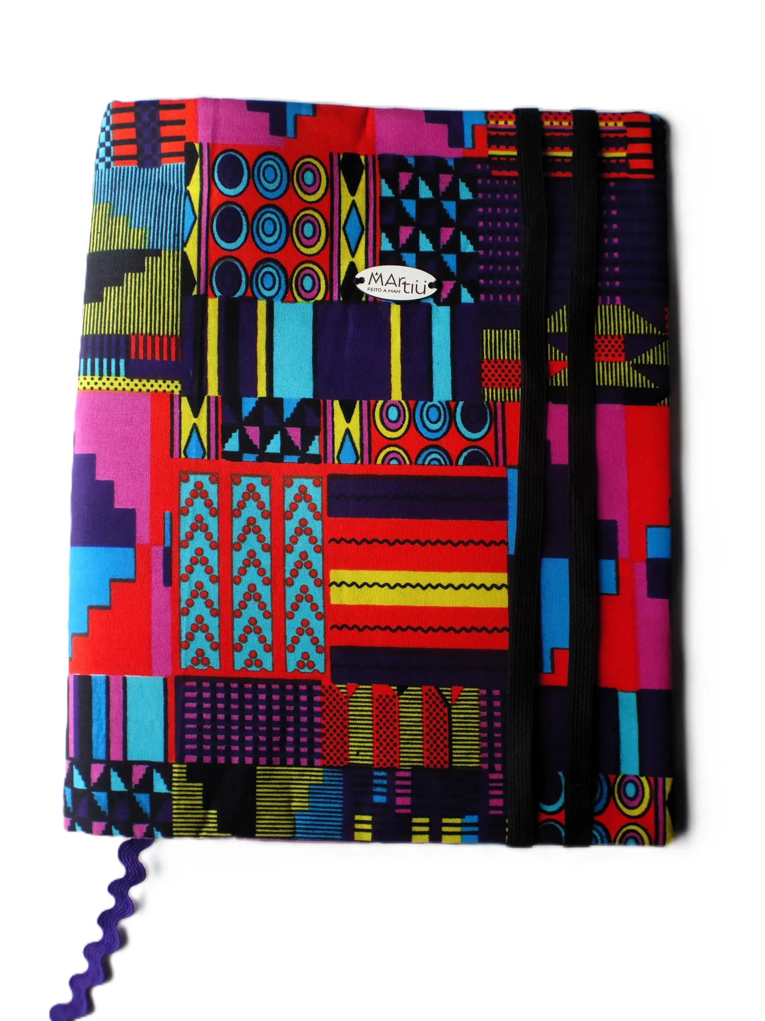 Funda protectora para agenda o cuaderno de la marca MARTIU con un diseño textil artesanal en colores vibrantes y patrones étnicos, que incluye un práctico cierre de doble cordón elástico para asegurar el contenido con el estilo distintivo de la marca.