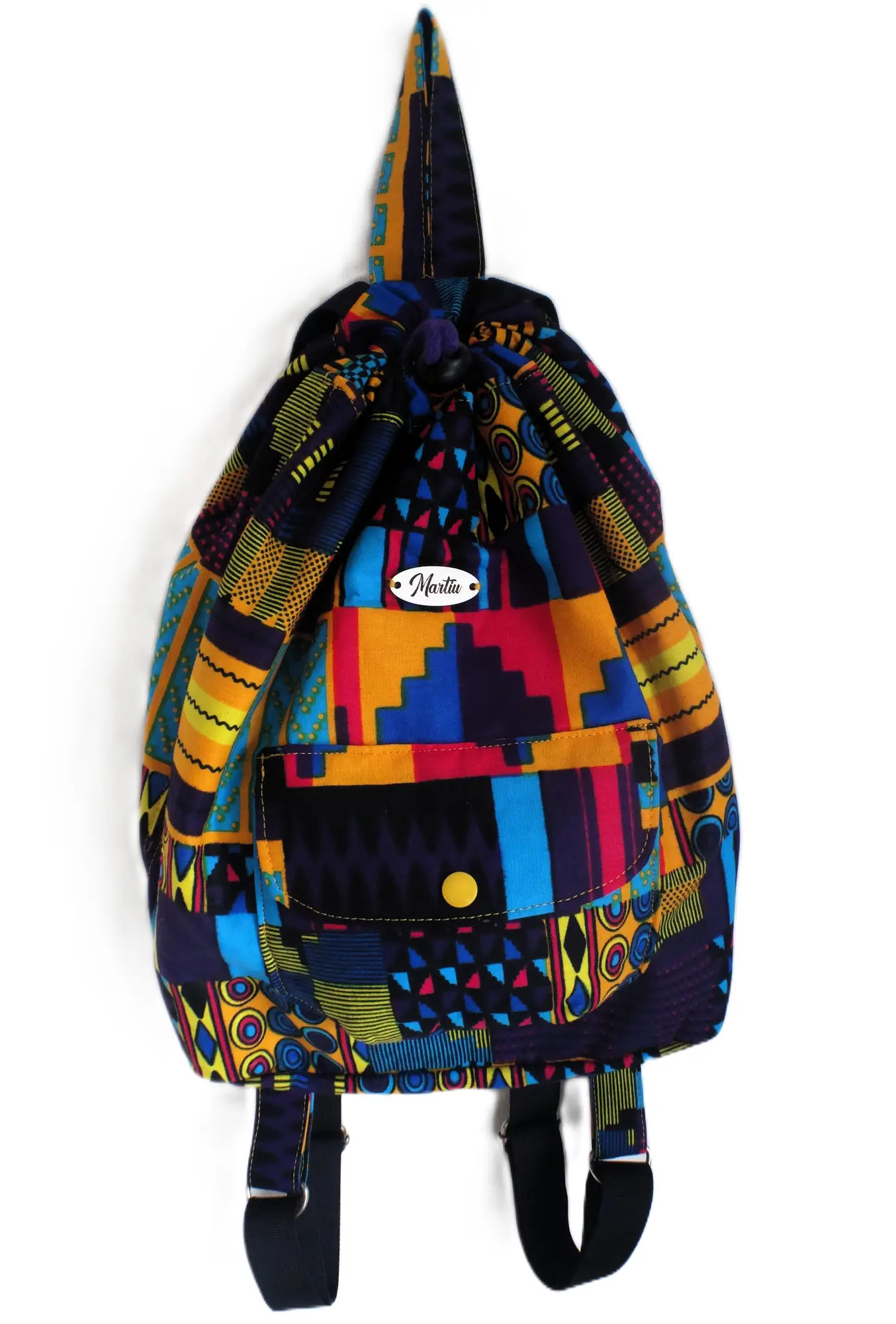 Una mochila tipo saco de la marca MARTIU que presenta un diseño vibrante con patrones geométricos multicolores, destacando el logotipo central y su confección artesanal única.